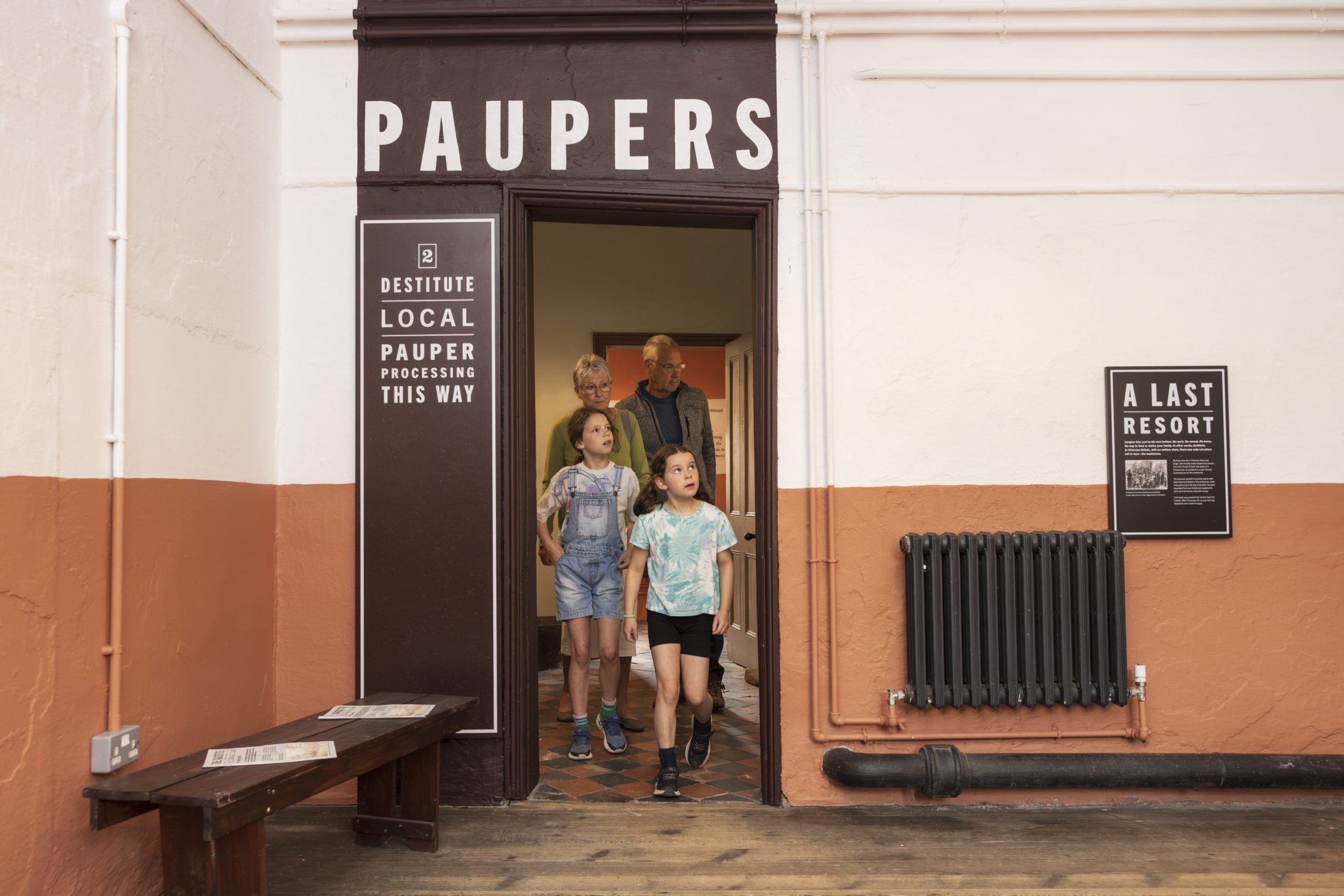 
							Children walk through a doorway with Paupers written above